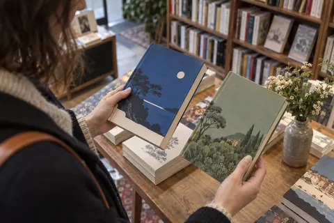 Illustration éditoriale : Lectrice comparant deux traductions d’une œuvre sur une table de librairie