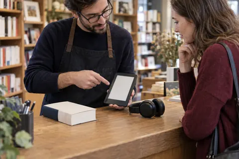 Illustration éditoriale : Libraire présentant un livre imprimé, une liseuse et un casque audio à une cliente